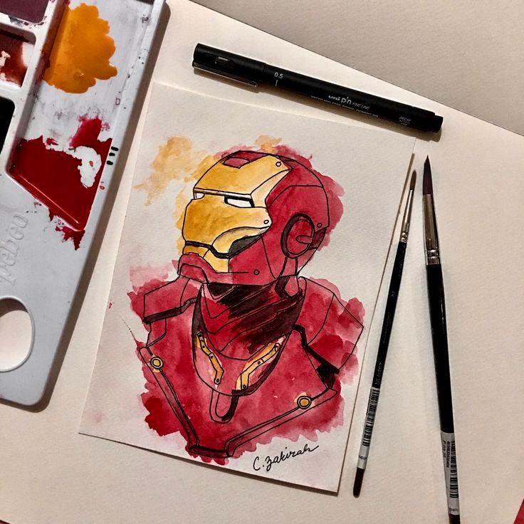 a drawing of iron man on paper next to paintbrushes and watercolor paints