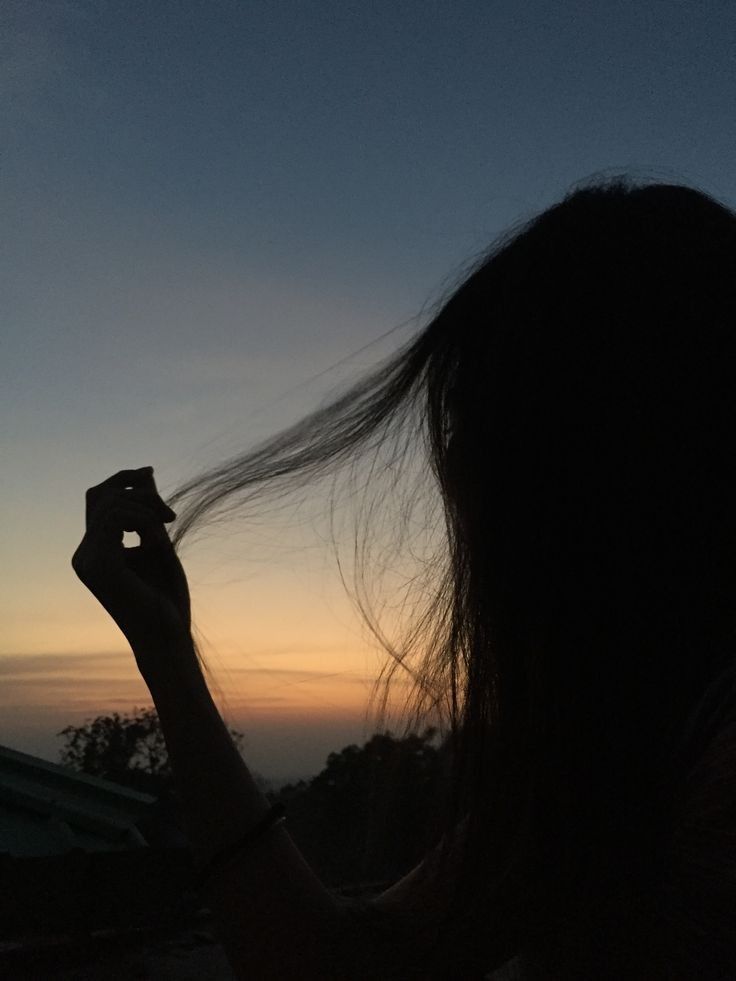 the silhouette of a woman holding her hair in front of an orange and blue sky