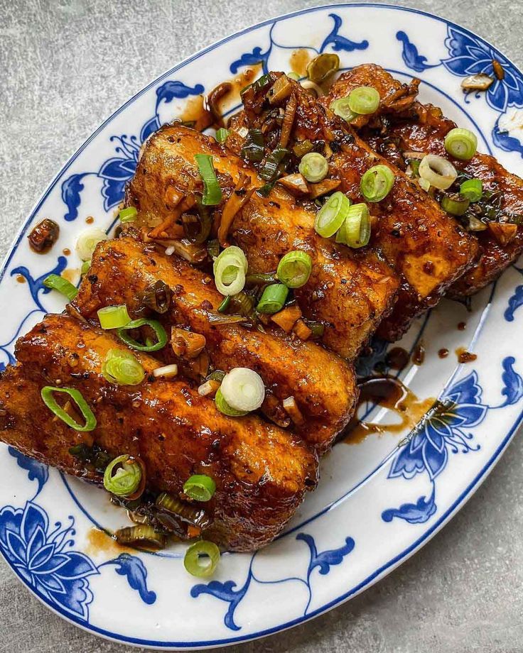 two pieces of chicken on a blue and white plate with green onion sprinkles