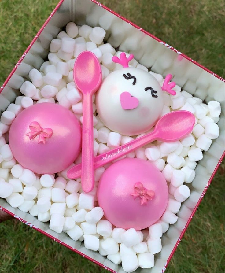 a box filled with pink and white marshmallows next to two spoons