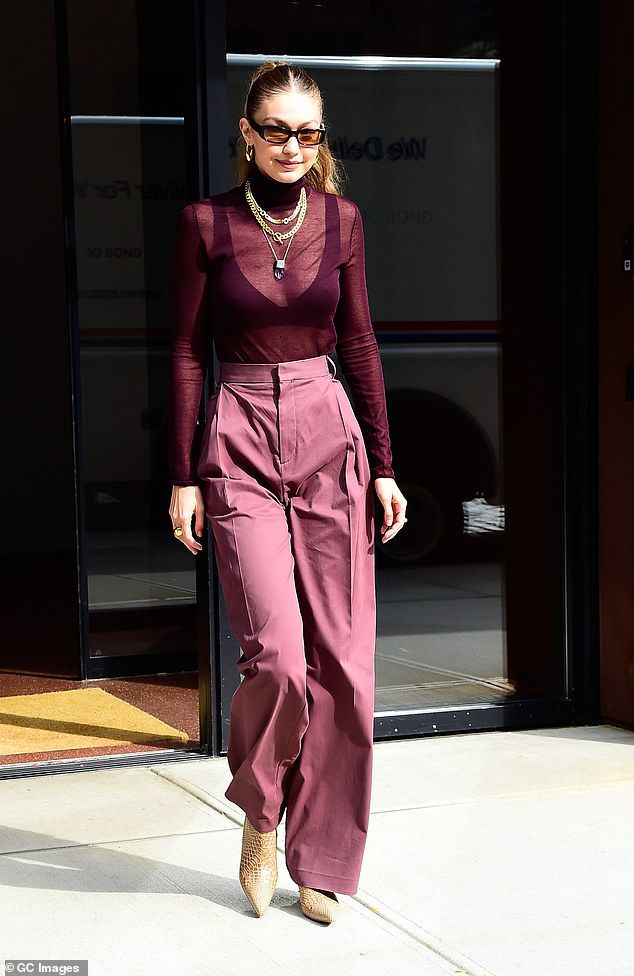 a woman walking down the street wearing purple pants and a maroon top with long sleeves