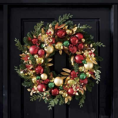 a christmas wreath on a black door with red, green and gold ornaments hanging from it