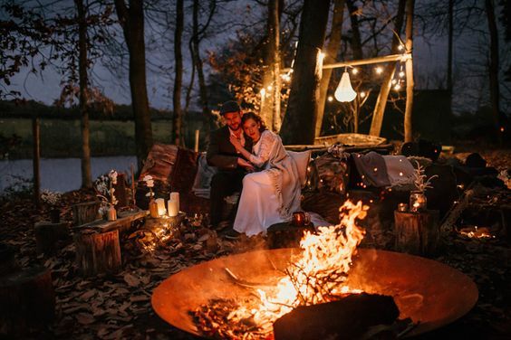 a couple sitting next to each other in front of a fire pit