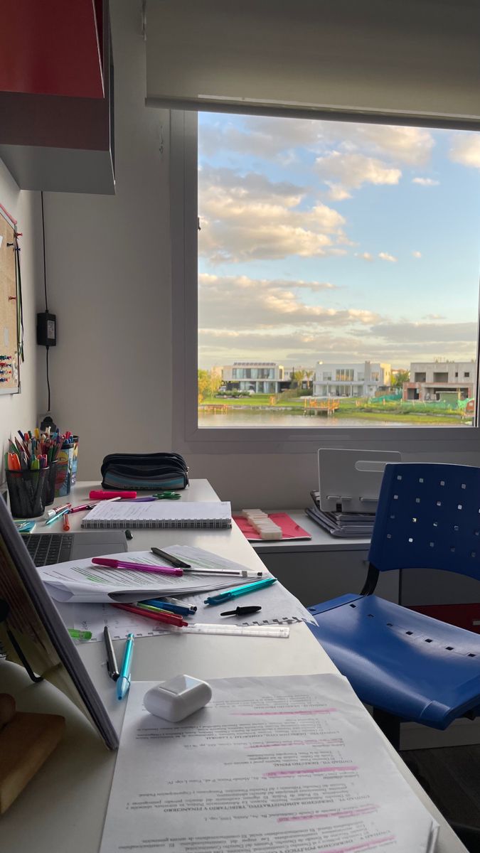 a desk with some papers on it and a blue chair in front of a window