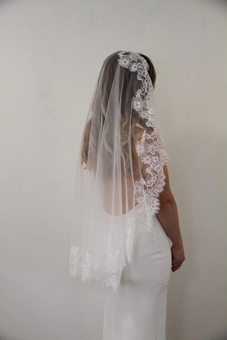 a woman in a wedding dress with a veil on her head is looking at the wall