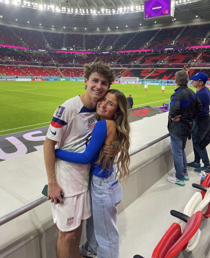 a man and woman are hugging in the stands at a soccer stadium with red chairs