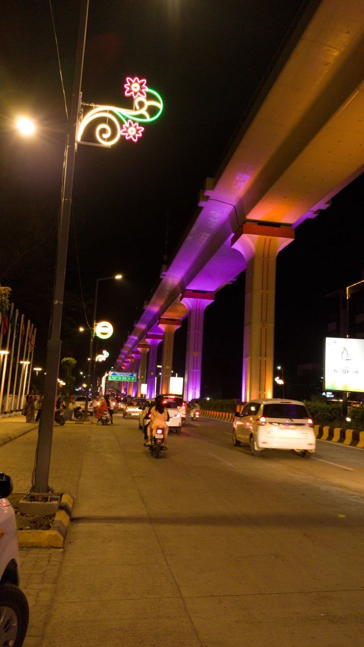 cars and motorcycles are parked on the side of an empty street at night with neon lights