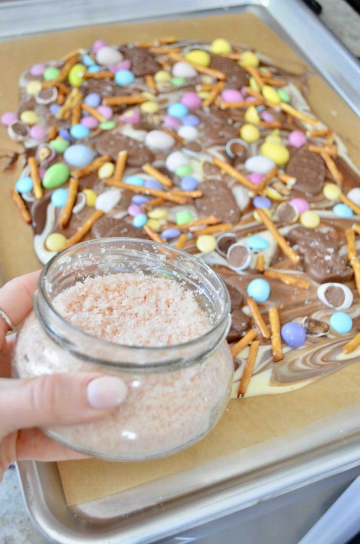 a person holding a jar filled with candy and pretzels on top of a cookie sheet