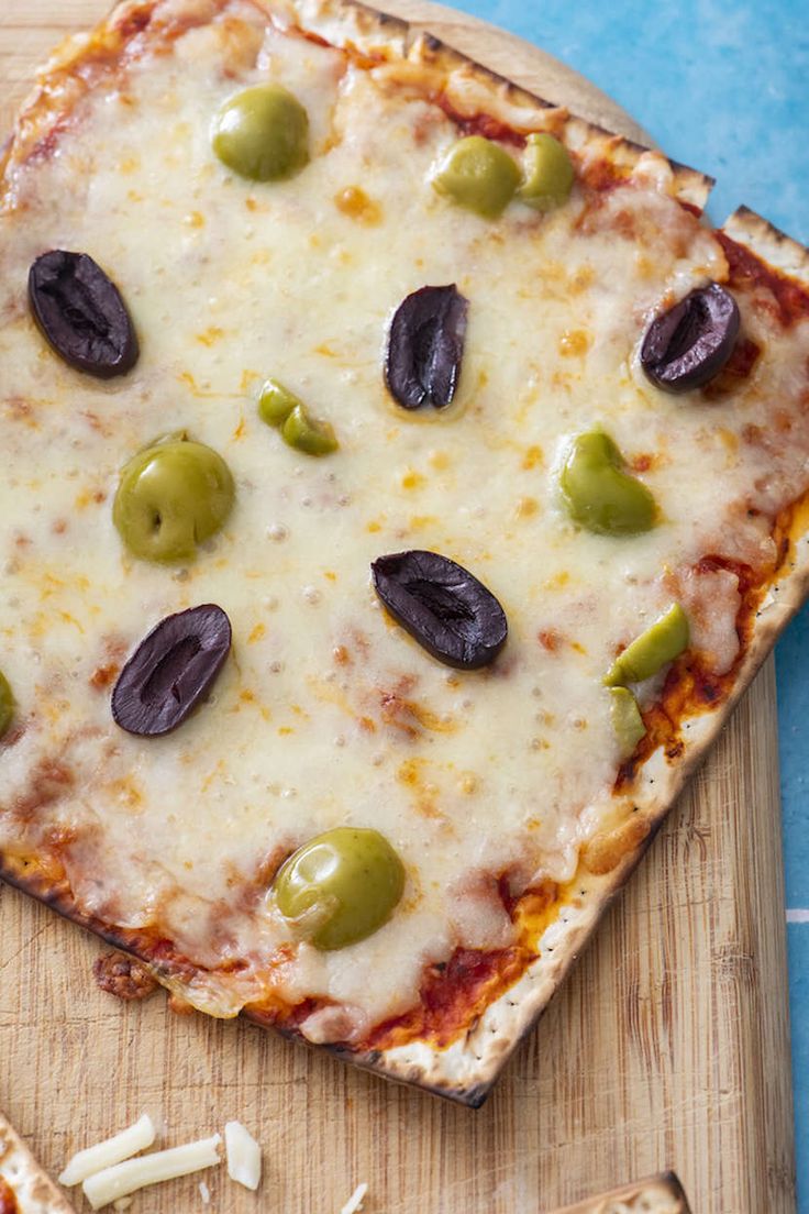 a square pizza with olives and cheese on a cutting board next to crackers