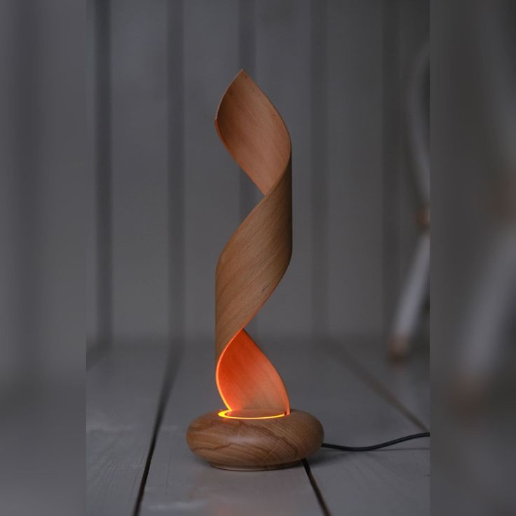 a wooden table lamp with an orange flame on it's side and a white wall in the background