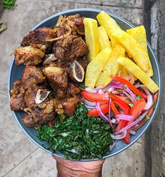 a person holding a plate with meat, vegetables and pineapple slices on it in their hand