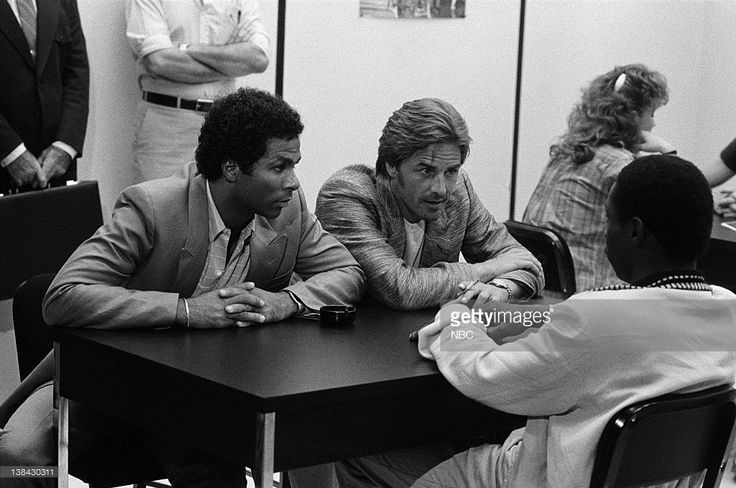 two men sitting at a table in front of other people and one man is looking at something