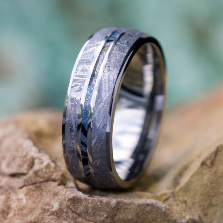 a wedding band with black and white wood inlays sits on top of a rock