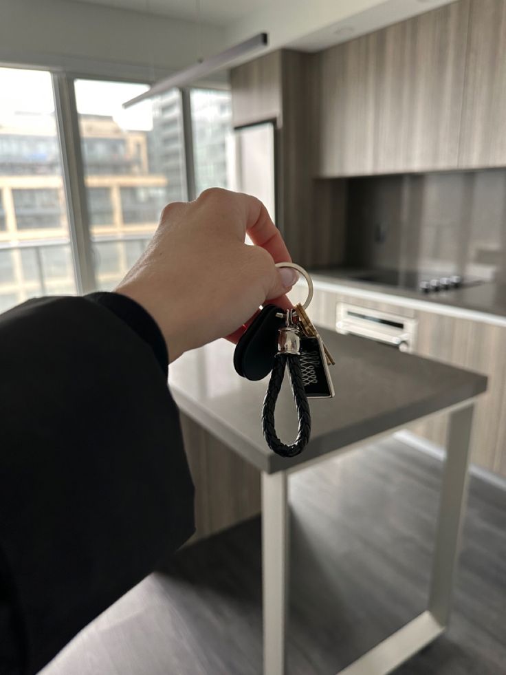 a hand holding a keychain in front of a table with a kitchen behind it