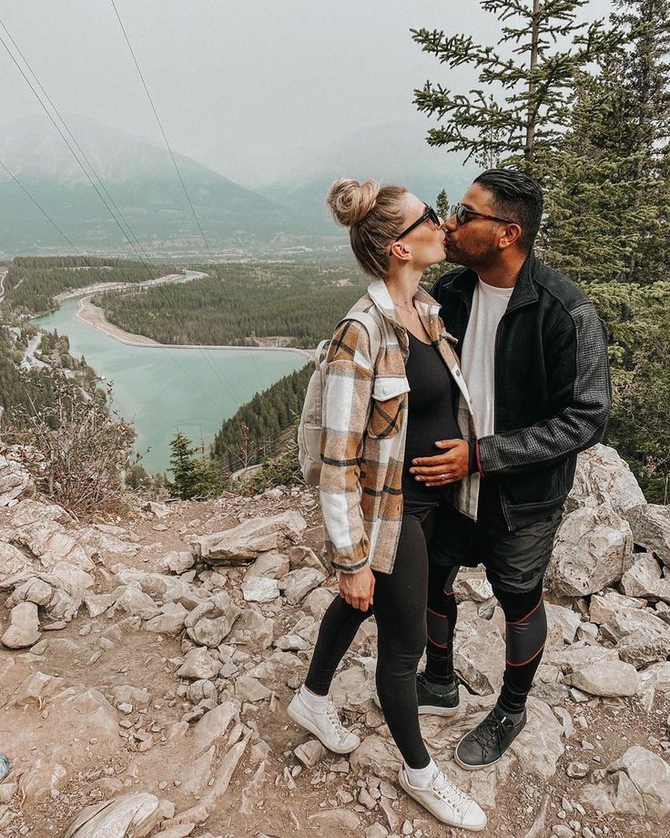 a man and woman kissing while standing on top of a rock covered hill next to a lake