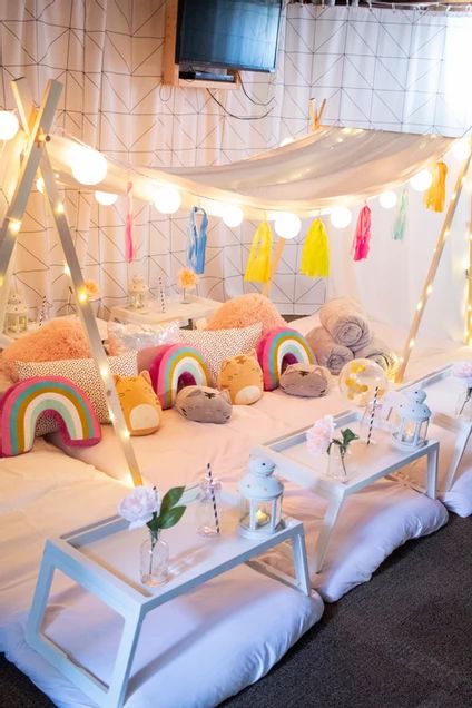 a bed with pillows and stuffed animals on it in a room that has lights strung from the ceiling