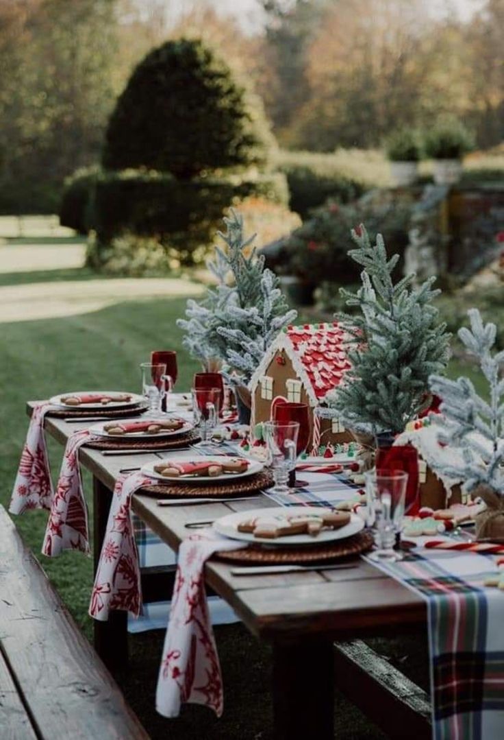 a picnic table set up for christmas with plates and napkins on it, trees in the background