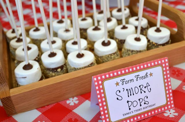 there are many marshmallows on sticks in the wooden tray with red and white checkered tablecloth