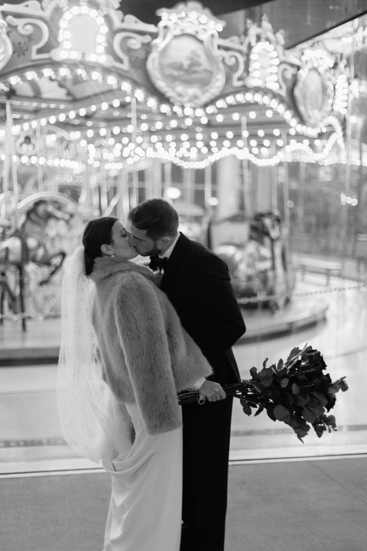 a bride and groom kissing in front of a merry - go - round at their wedding