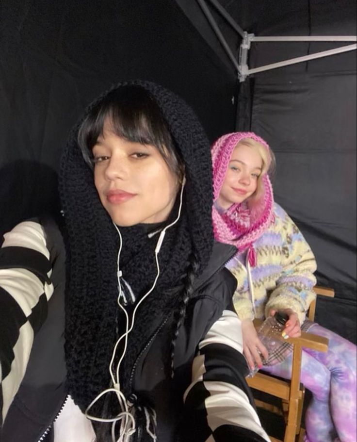 two women sitting next to each other in front of a black tent with headphones on