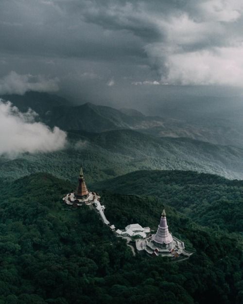 an aerial view of a pagoda in the middle of a forest with mountains and clouds