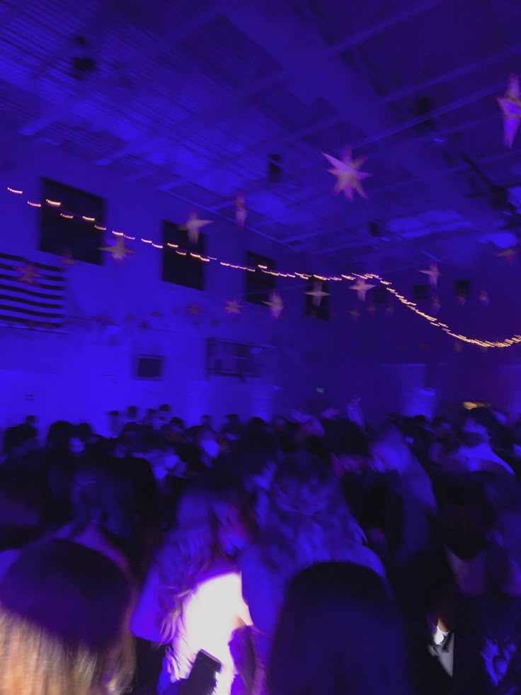 a large group of people in a room with purple lighting and stars on the ceiling