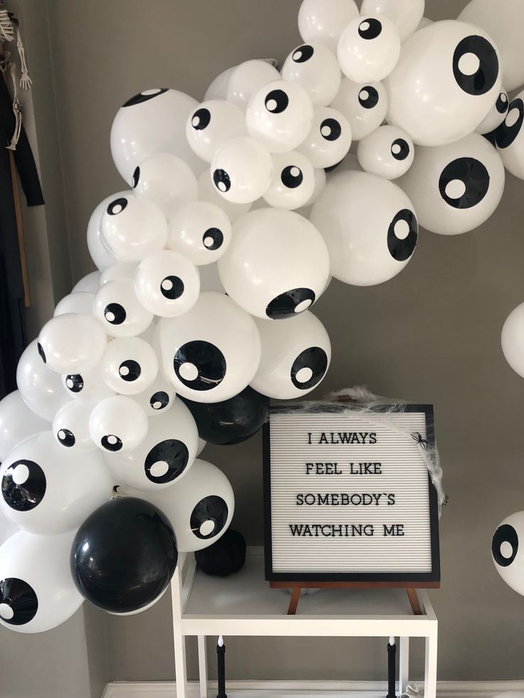 balloons with black and white eyes are hanging from the ceiling above a sign that says i always feel like somebody's watching me