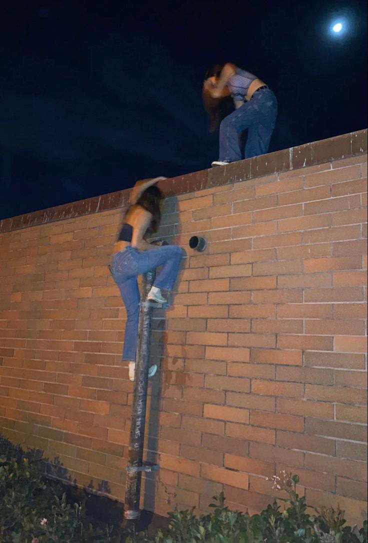 two people climbing up the side of a brick wall