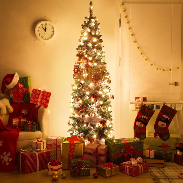 a christmas tree with presents under it in front of a wall clock and stockings on the floor