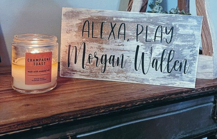 a candle sits next to a wooden sign that says, alexaplay morgan walter