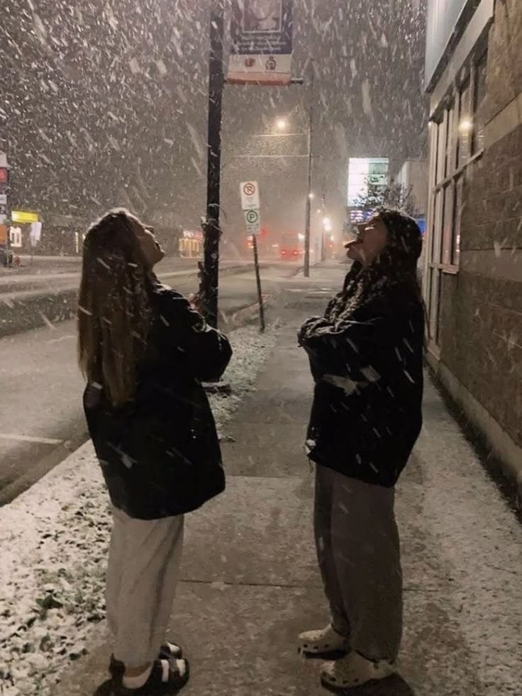 two women standing on the sidewalk in the snow looking at each other with their eyes closed