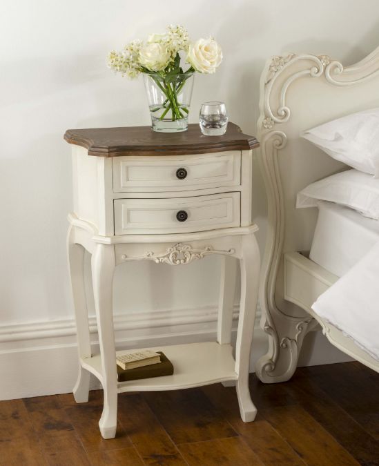 a small white table with flowers in a vase on top of it next to a bed