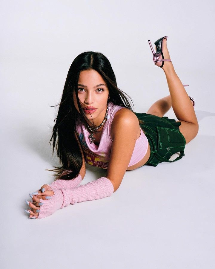 a woman laying on the ground with her legs spread out and wearing pink gloves, holding a pair of high heeled shoes