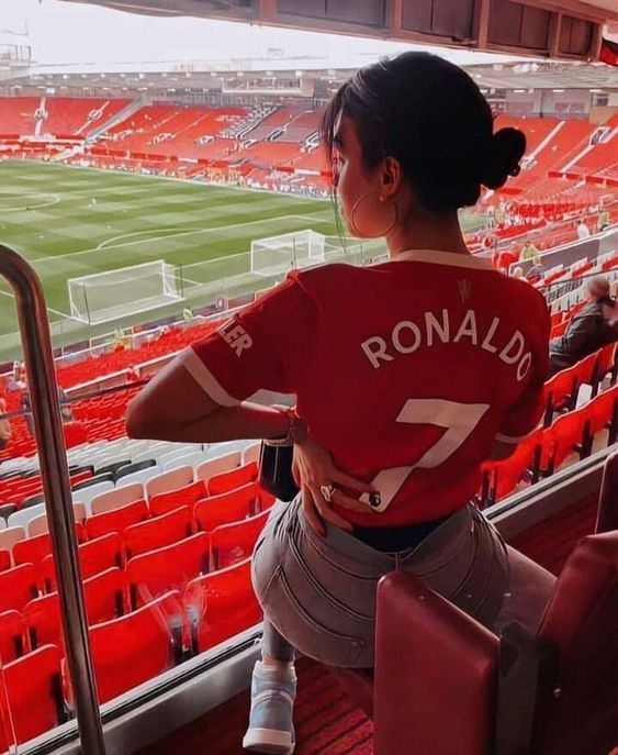 a woman sitting in the bleachers at a soccer stadium with her back to the camera