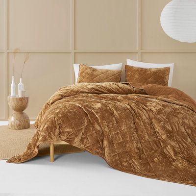 a bed with a brown comforter on top of it next to a vase and lamp