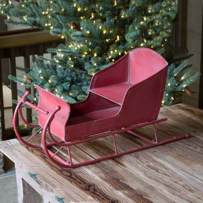 a red sleigh sitting on top of a wooden table next to a christmas tree