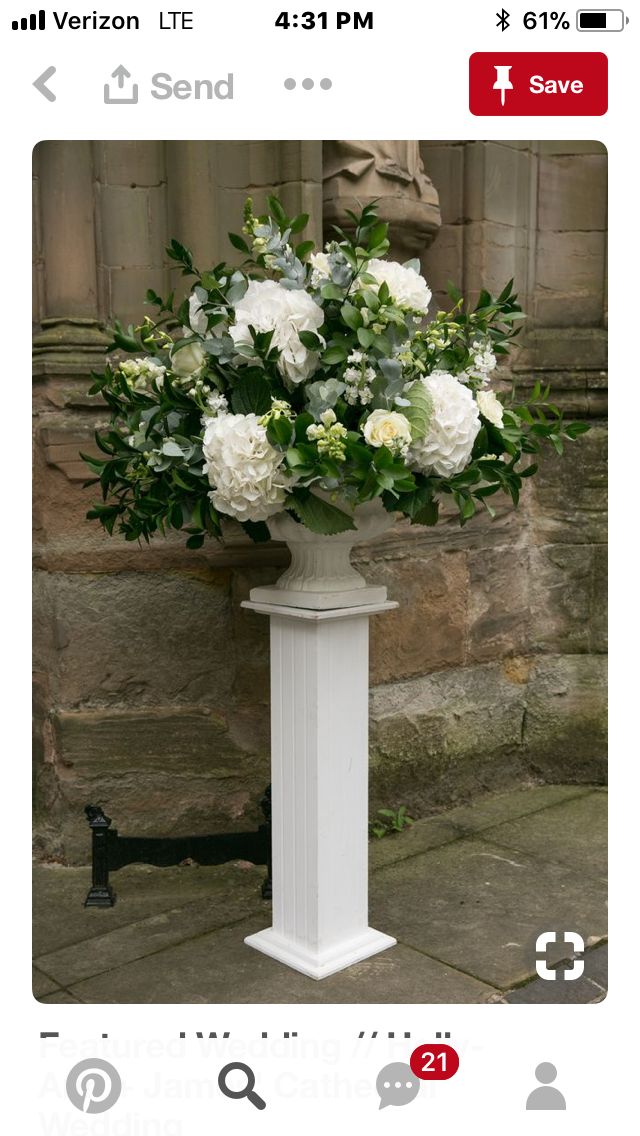 a white vase filled with lots of flowers on top of a sidewalk next to a stone wall