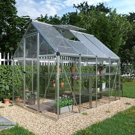 a small greenhouse in the middle of a yard with potted plants and flowers inside