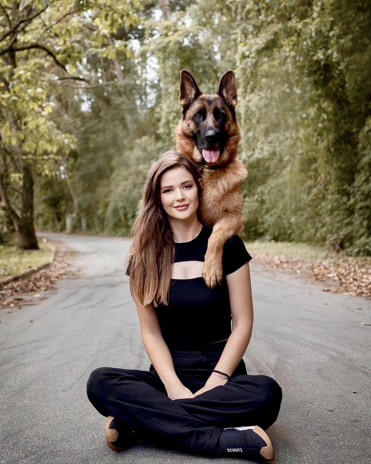 a woman sitting on the ground holding a dog over her shoulder and smiling at the camera