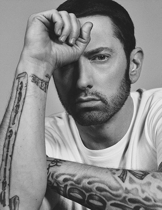 a black and white photo of a man with tattoos on his arms, looking at the camera