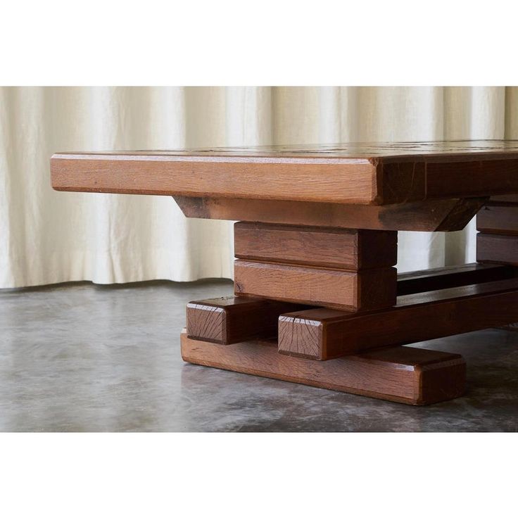 a wooden table sitting on top of a cement floor next to a curtained window