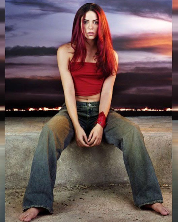 a woman with red hair is sitting on a concrete ledge and looking at the camera