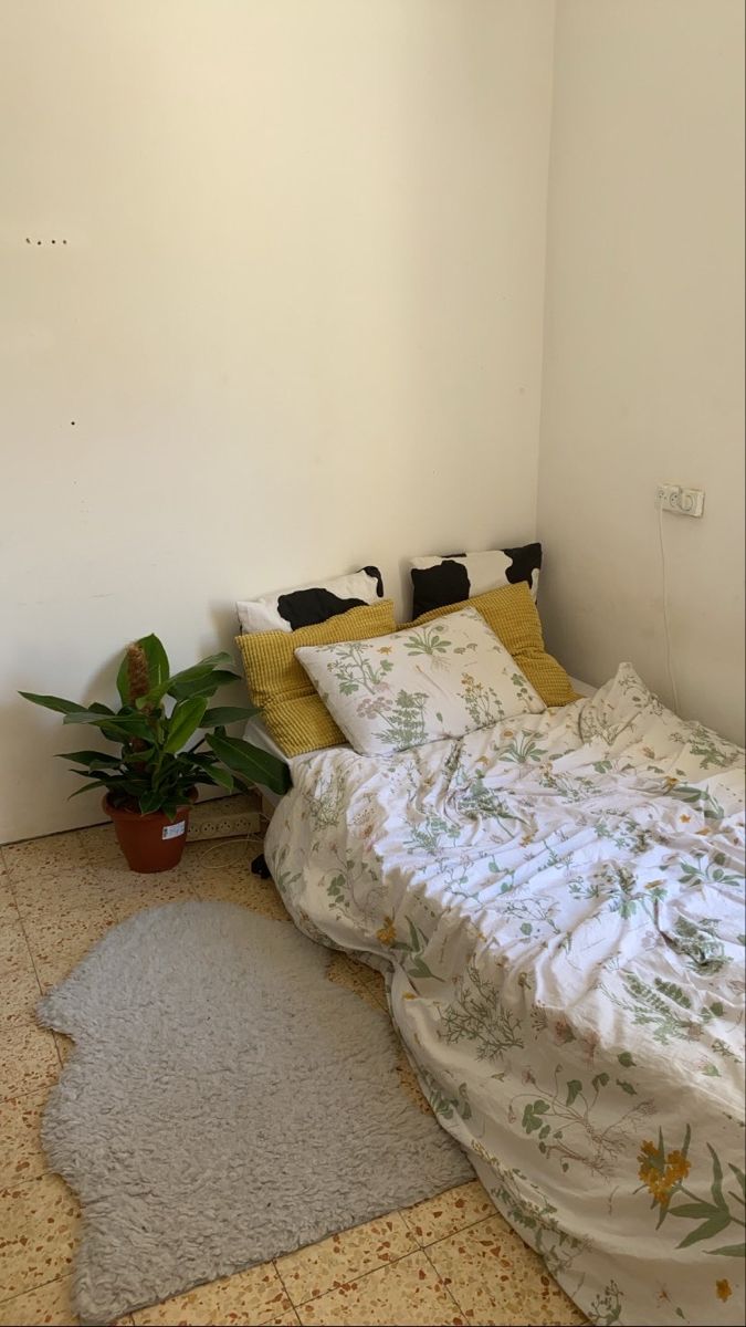 a bed sitting next to a potted plant on top of a white wall in a bedroom