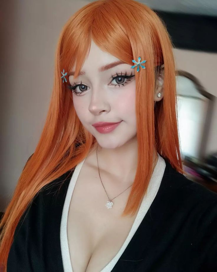 an orange haired woman with long hair and piercings on her ears is posing for the camera