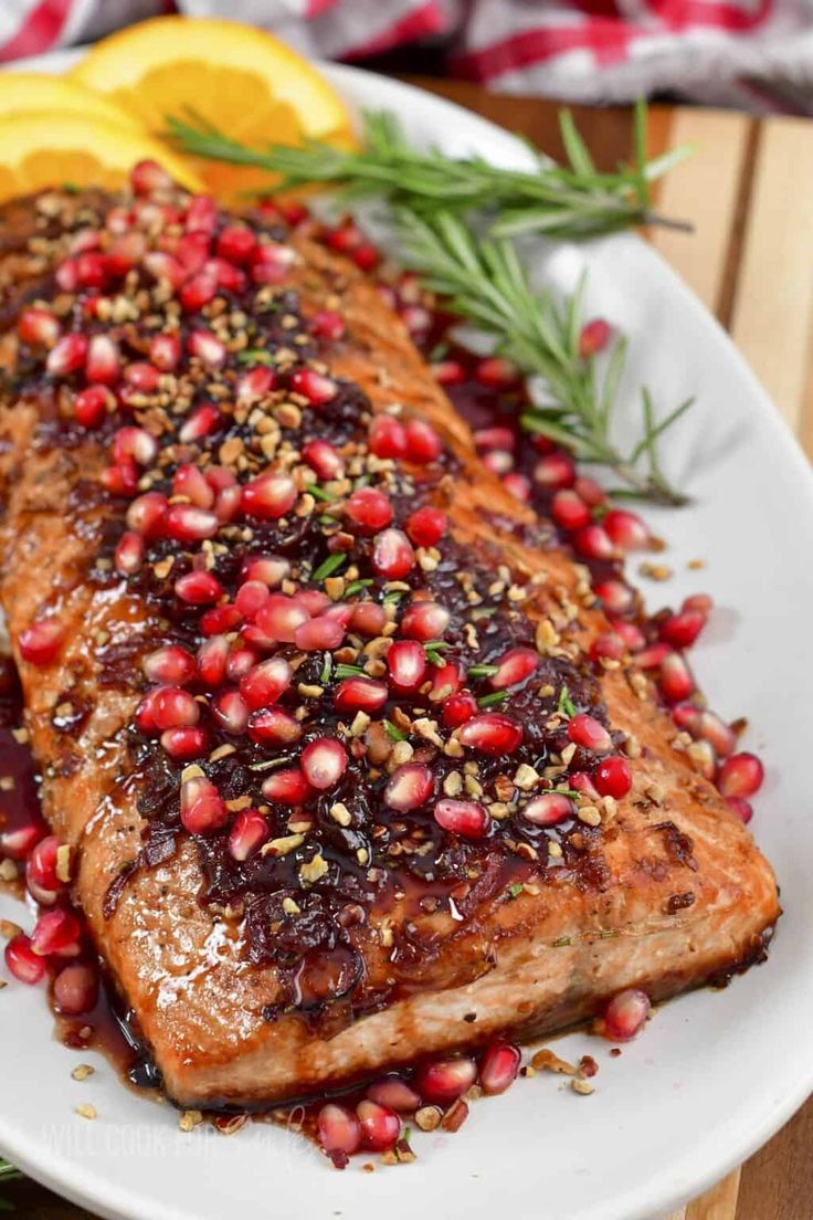 a white plate topped with meat covered in pomegranates and garnish