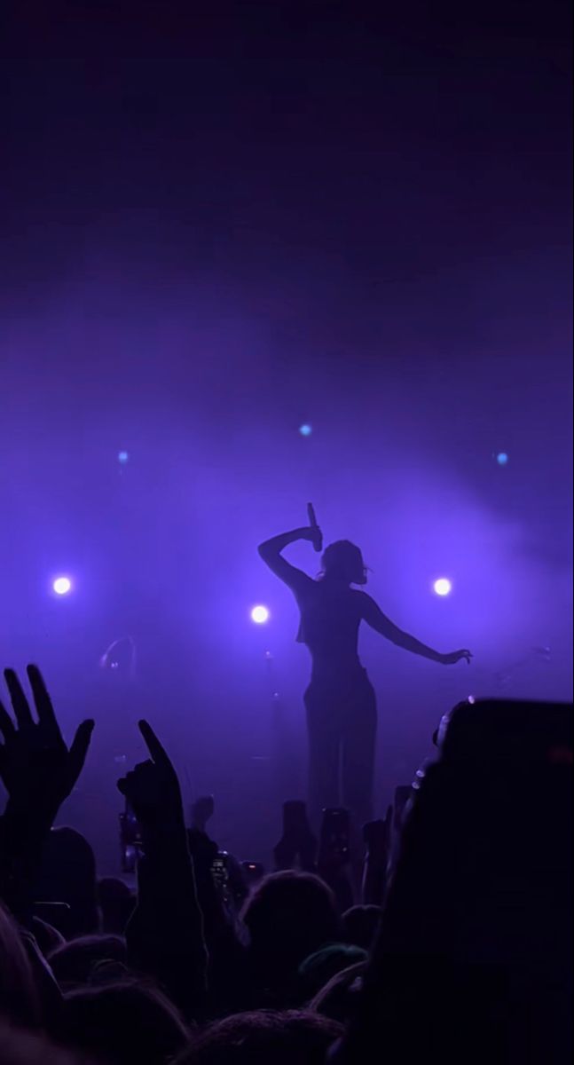 a woman standing on top of a stage with her arms raised in the air and lights behind her