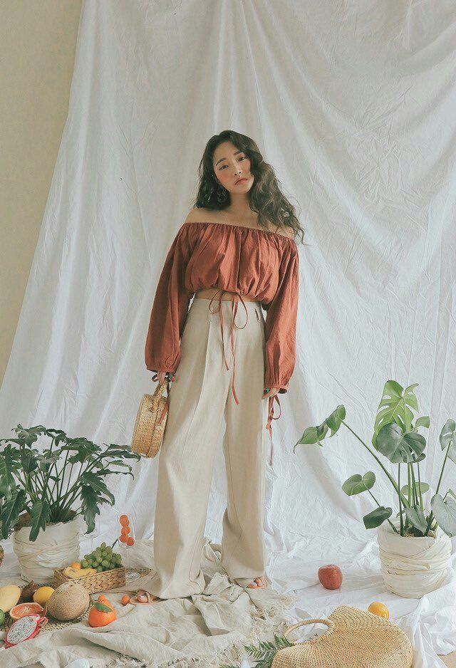 a woman standing in front of a white backdrop with potted plants and other items