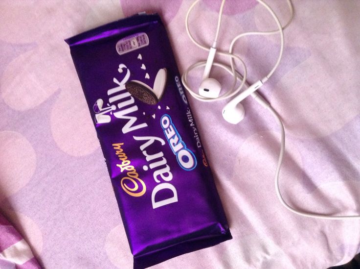 a bar of dairy milk next to headphones on a bed