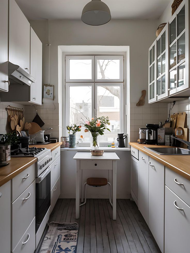 a kitchen with white cabinets and wooden flooring next to an open window overlooking the street