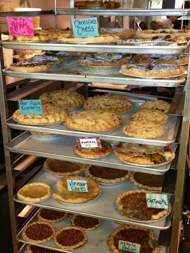 many pies are sitting on the shelves in a display case, with price signs